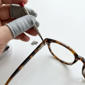 Close-up of a hand using a precision tool from a reading glasses repair kit to fix a loose hinge.